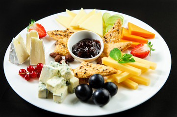 Platter with different types of cheese, fresh fruits and sauce