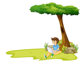 Obraz na płótnie Canvas A boy using his laptop under a tree