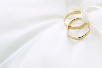 Gold wedding rings on white ring pillow with copy space. Wedding invitation background. 