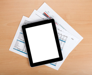 Tablet with blank screen over papers with numbers and charts