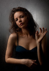 Portrait of a girl behind wet glass on a gray background.