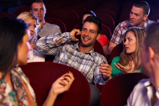 Confident young man using mobile in cinema