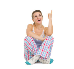 Happy young woman in pajamas sitting and pointing on copy space