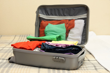 Open grey suitcase with clothing on bed