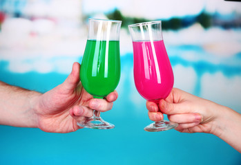 Cocktails in men's and women's hands on pool background