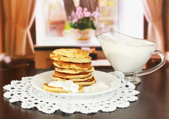 Sweet pancakes on plate with sour cream on table in room