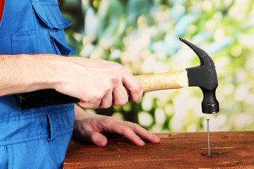 Builder hammering nails into board on natural background