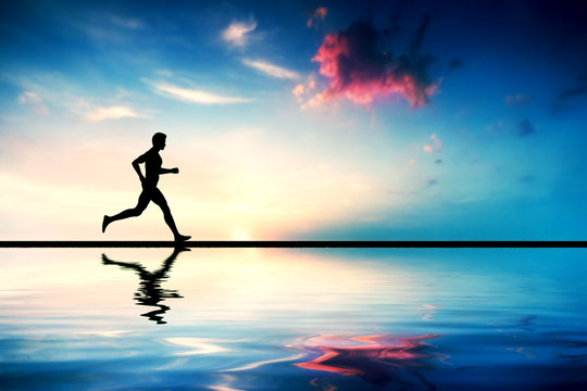 Silhouette of man running at sunset. Water reflection