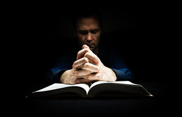 Man praying to God with his hands resting on a bible.