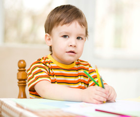 Little boy is drawing on white paper
