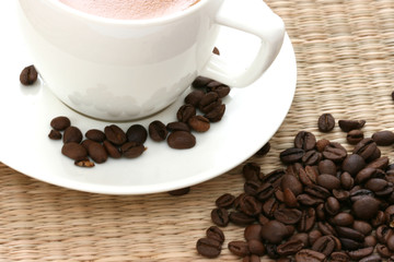 Whole coffee beans scattered with white cup