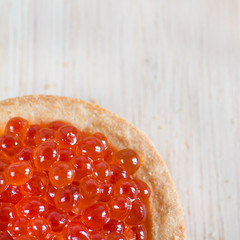 Tartlet with red caviar on light wooden background