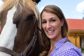 Obraz premium Young woman in the stable with horse in sunshine