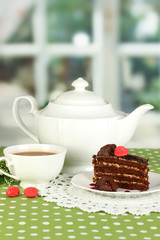 Teapot, cup of tea and delicious cake on window background