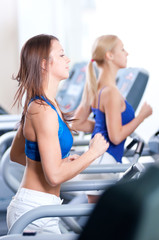 Obraz na płótnie Canvas Two young women run on machine in the gym