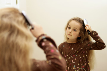 Cute little girl brushing hair while looking in the mirror