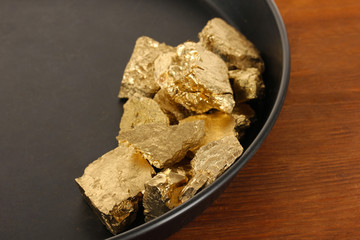 Gold pan with golden nuggets inside on wooden background