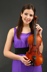 Beautiful young girl with violin on grey background