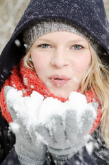junge blonde Frau pustet in einen handvoll Schnee