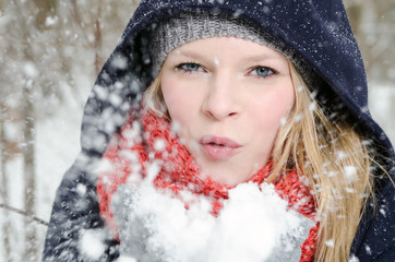 junge blonde Frau pustet in einen handvoll Schnee