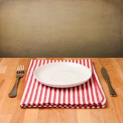 Empty plate with silverware on tablecloth on wooden table