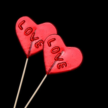 Two red heart shaped lollipops on black background.