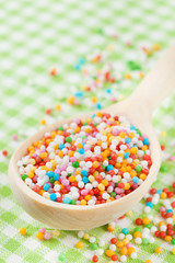 colorful sugar sprinkles in wooden spoon on tablecloth