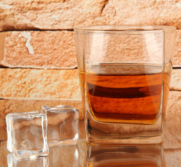 Glass of whiskey and ice on brick wall background