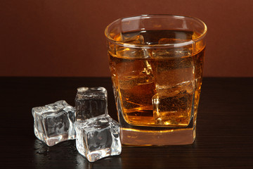 Glass of whiskey and ice on brown background