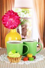 Cups of tea with cake,candy and flower on table in room