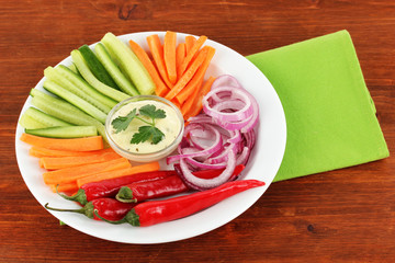 Assorted raw vegetables sticks in plate on wooden table close