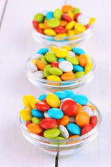 Colorful candies in glass bowls on white wooden background