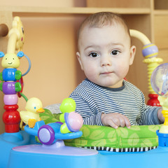 Cute  baby in a walker or bouncer with toys.