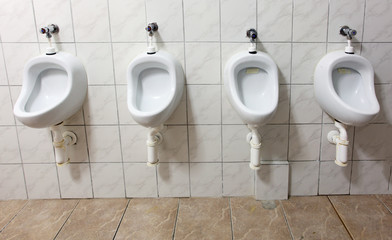 line of white porcelain urinals in public toilets