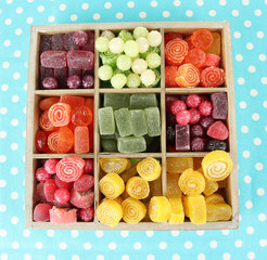 Multicolor candies in wooden box, on color background