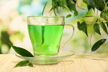 Transparent cup of green tea on bamboo mat, on nature