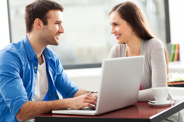 Obraz na płótnie Canvas Couple talking and using laptop at cafe