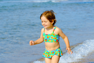 Happy toddler girl running on the beach