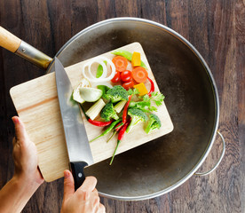 Fresh vegetables on the cutting board are falling in the wok. Co