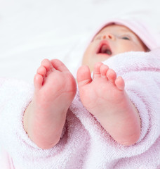 A close-up of tiny baby girl feet on pink cotton towel.