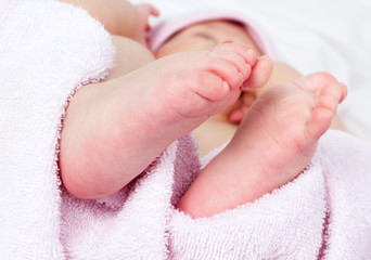 A close-up of newborn baby girl feet on soft pink cotton towel