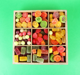 Multicolor candies in wooden box, on color background