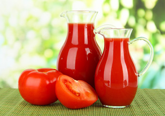 Tomato juice in pitchers on table on bright background