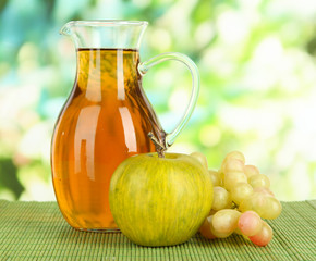 Apple juice in pitcher on table on bright background