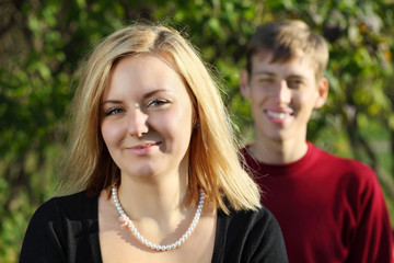 Young happy woman and man behind her in park at sunny autumn day