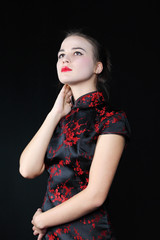Young girl in Japanese silk blouse looks up at black background.