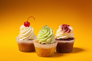 three cupcakes isolated on orange background with copyspace