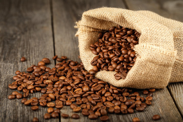 Coffee beans in coffee bag made from burlap on wooden surface.