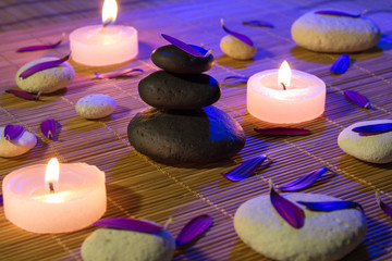 white and black stones, purple petals, and candles on bamboo