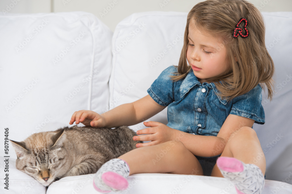 Wall mural cute little girl hugging tabby cat with love, looking at cat.